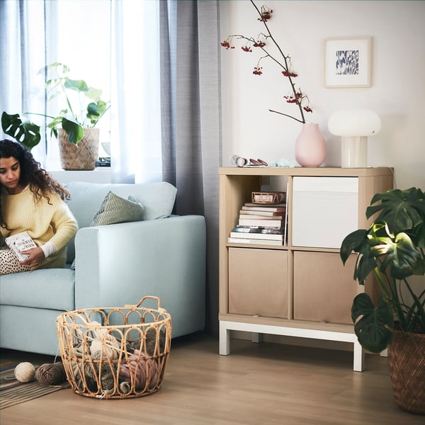 Person reading in cosy living room, KALLAX shelf, yarn basket, and plants.