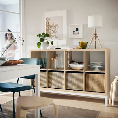Modern living room with KALLAX wooden shelf unit, blue chairs, lamp, and decorative items.
