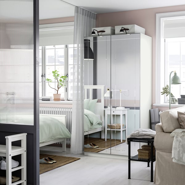 Modern bedroom with KAMMARTORP white mirrored wardrobe, cosy bed, windows, sofa, side table, and shelves.