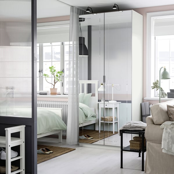 Modern bedroom with mirror door, reflecting bed and room, creating spacious feel. White door complements light decor with green bed and beige sofa.