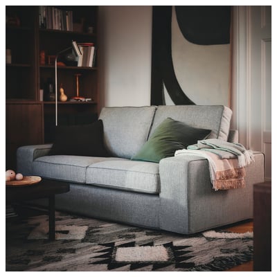 Cosy grey KIVIK sofa with black & green pillows, large & comfy, fits well in room with bookshelf.
