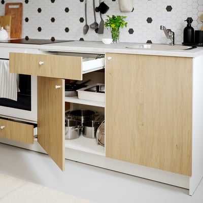 Modern kitchen with wood cabinet, open drawer, pans, marble countertop, and sink.