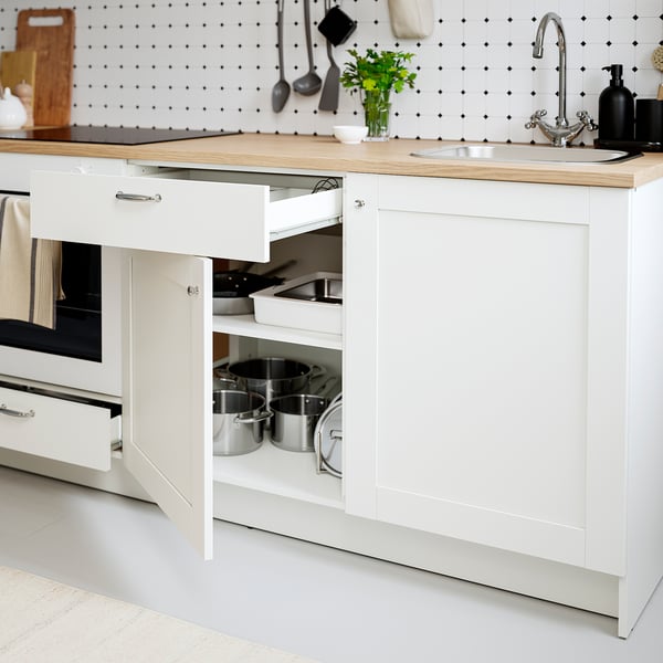 Kitchen storage with open drawer showing pots; white cabinets, oak countertop, black and white backsplash.