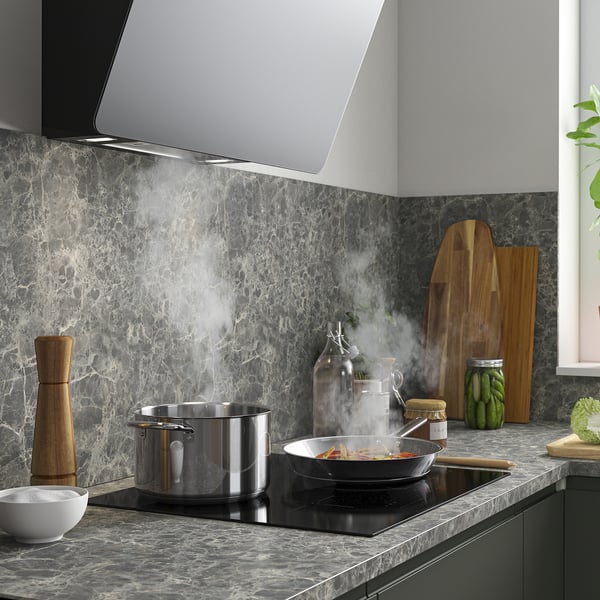 Modern kitchen with induction stove and pots cooking. Stainless hood, marble backsplash, and wooden boards.