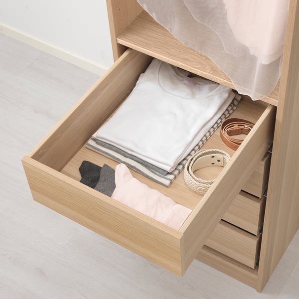 Open wooden drawer with folded clothes and accessories, part of IKEAs KOMPLEMENT storage system.
