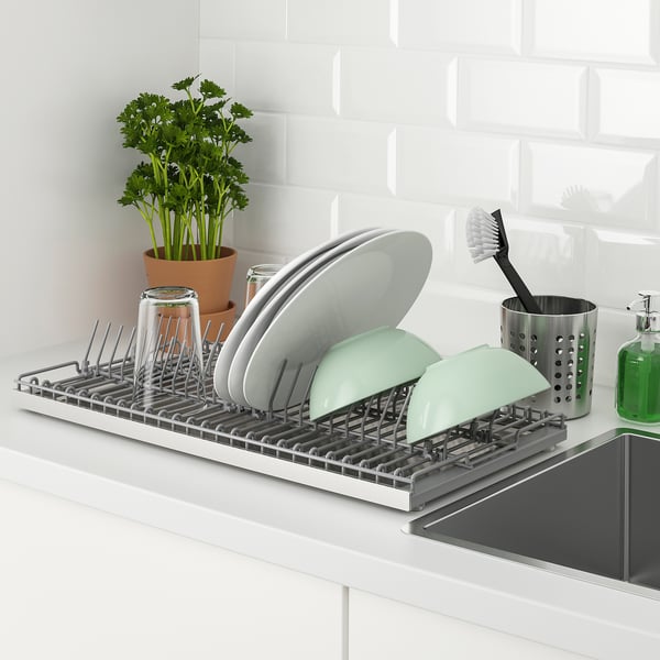 Kitchen dish drainer on counter stores washed items. Holds plates, cups, and cutlery, with a removable tray for collecting water.