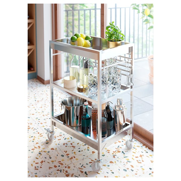 Metal bar cart with wheels, shelves, glasses, bottles, and fruit. Modern design.