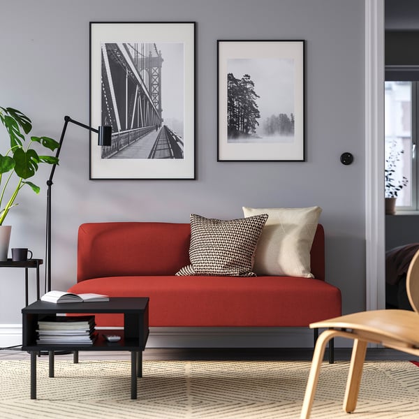 Modern living room with red LILLEHEM sofa, pillows, black coffee table, plant, lamp, and photos on grey wall.