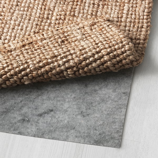 Close-up of textured natural jute rug over grey felt backing on floor.