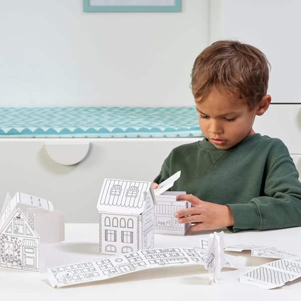 A young boy is crafting with the MÅLA cardboard house templates, developing fine motor skills and creativity by assembling and colouring a small town.