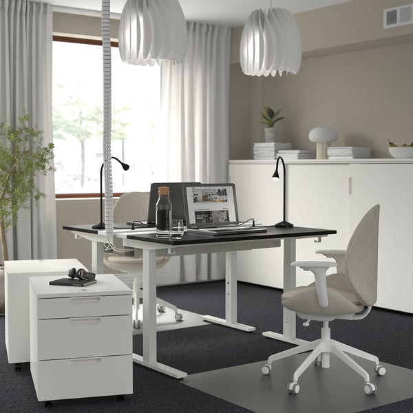 A modern office setup with a MITTZON white standing desk, a grey office chair, a laptop, and a bottle, all arranged neatly.