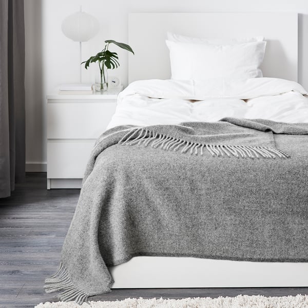 Minimalist bedroom featuring a white bed with a cosy, textured grey wool throw blanket neatly folded at the foot.