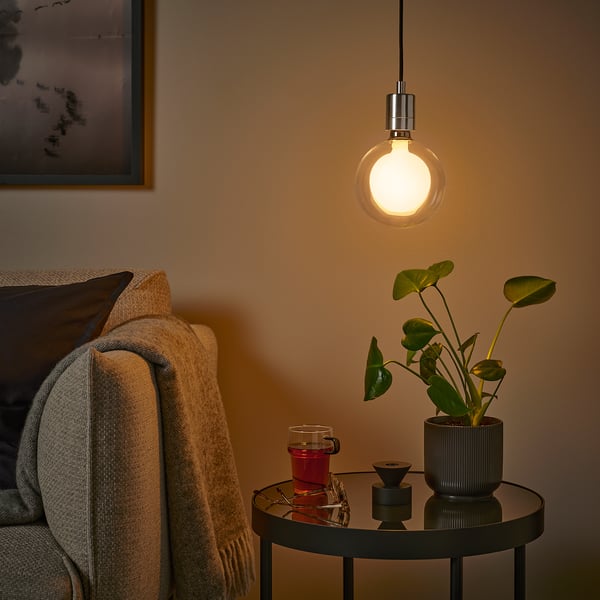 Cosy corner: hanging bulb, beige throw, glass table, warm light.