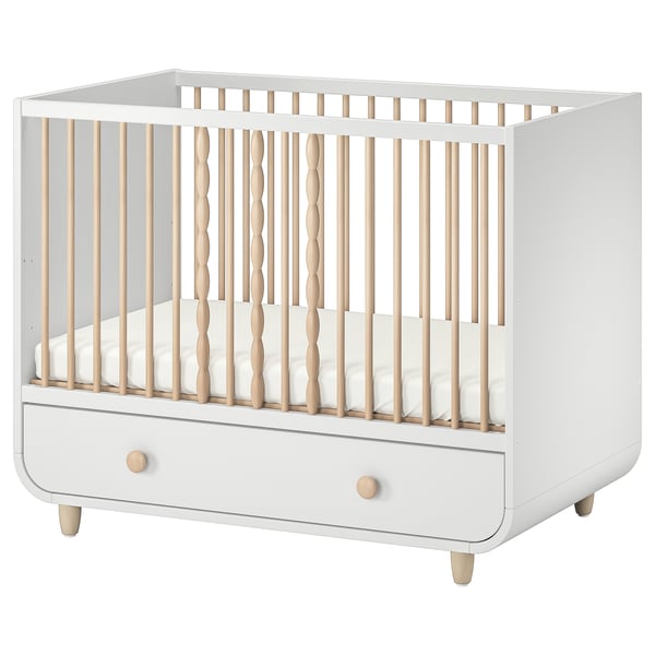 A white and light wood MYLLRA cot with a drawer for a babys room.
