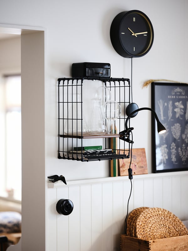 Modern room with black clock, glassware shelf, and clamp lamp on beadboard wall.
