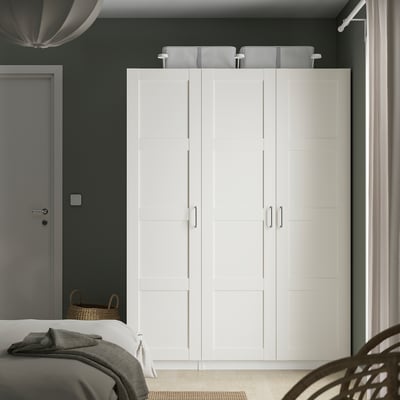 A large white PAX wardrobe in a bedroom, taller than the bed and door beside it, with sleek panels and handles.