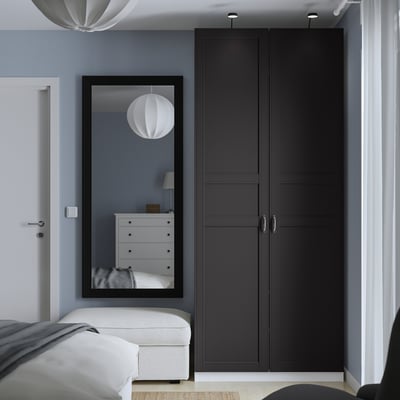 Modern black double-door wardrobe beside mirror, against blue wall.