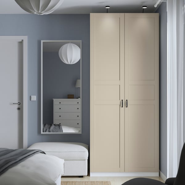 Modern bedroom with tall beige PAX wardrobe, mirror, and white drawers.