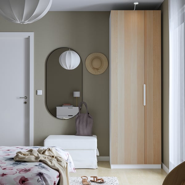 Modern bedroom with tall, light wood PAX wardrobe, white dresser, round mirror, and floral bedding.