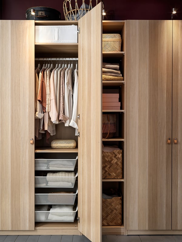 A modern wooden PAX closet with open doors, displaying neatly organised shelves and drawers in light brown colour.