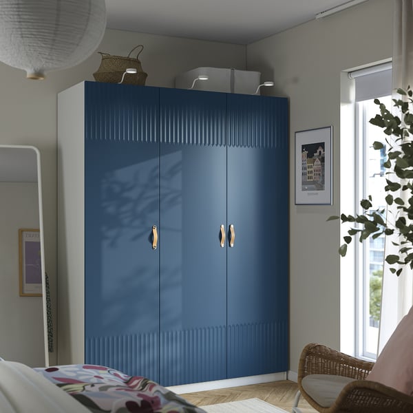 Modern bedroom with large blue PAX wardrobe, flowers bed, wicker chair, and wall art.