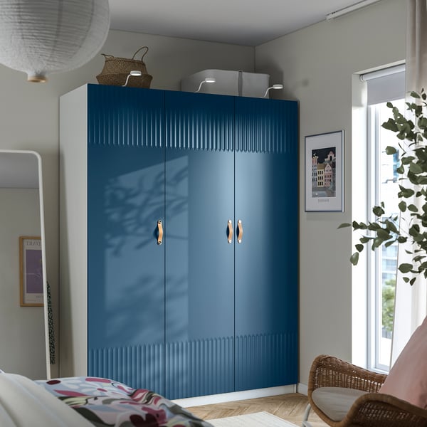Large blue PAX wardrobe in bedroom, with patterns on bed, chair, and wall decorations, achieving a stylish and organised look.