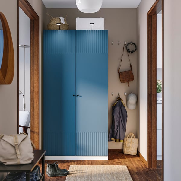 Modern hallway with tall blue PAX wardrobe, hooks with jacket, hat, and headphones, enhancing room organisation.