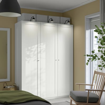 A well-organized bedroom corner with a large ikea PAX wardrobe, sleek handles, mirror, and wooden rocking chair.