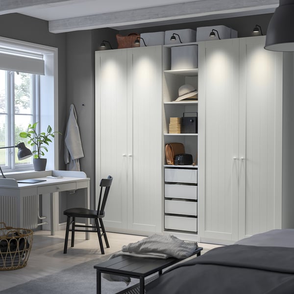 Modern bedroom with large white wardrobe, black accents, shelves, drawers, lighting, desk, chair, and blinds.
