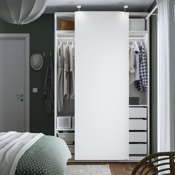 A modern bedroom with an open PAX wardrobe displaying clothes hangers, drawers, and shelves. Clothes and accessories are neatly organised.
