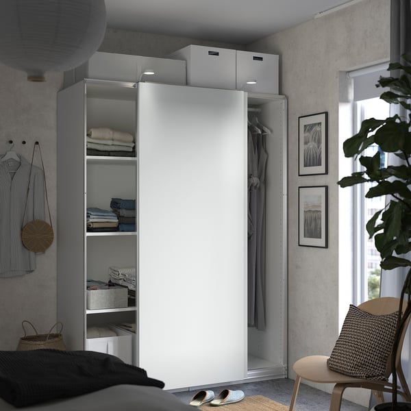 Modern bedroom with white PAX wardrobe, grey clothes, plant, chair, sandals, and art.