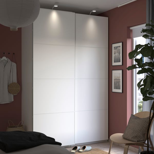Modern minimalist bedroom with large white wardrobe, red walls, and large window.