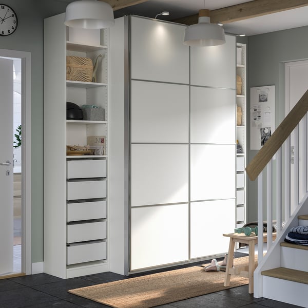 Modern white PAX wardrobe with sliding doors, drawers, shelves, and decorative lights.