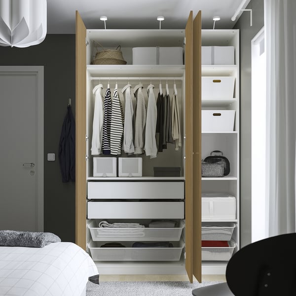 Open wardrobe displaying clothes, drawers, and storage boxes inside; part of a bedroom setup.