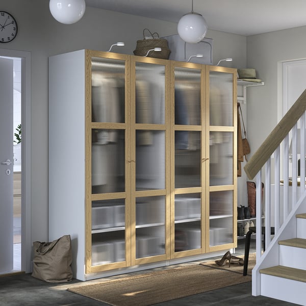 Large wooden PAX wardrobe with glass doors, positioned beside white stairs. Light grey walls, rug under.