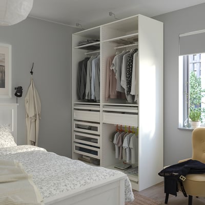 Organised bedroom with large PAX wardrobe, hanging clothes, drawers, floral bedspread, chair, and coat.