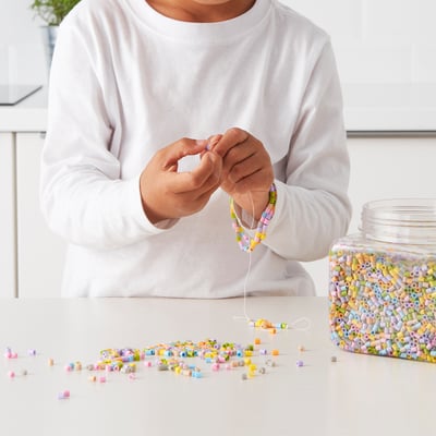 Person threading colourful beads to make jewellery. Beads in jar, string in use, craft project in progress.