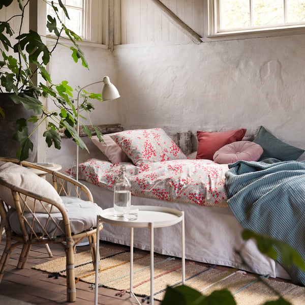 Cosy, rustic room with floral bed, pink pillows, wicker chair,elsewhere, RAKLEV rug - colourful, woven jute/wool blend, soft, earthy.