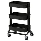 A black, three-tiered utility cart, RÅSKOG, with metal frames and plastic bins for storage and mobility.