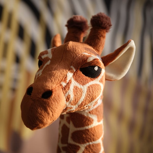 Stuffed giraffe toy, soft, detailed with brown and white patches, two small horns, long neck, lifelike eyes.