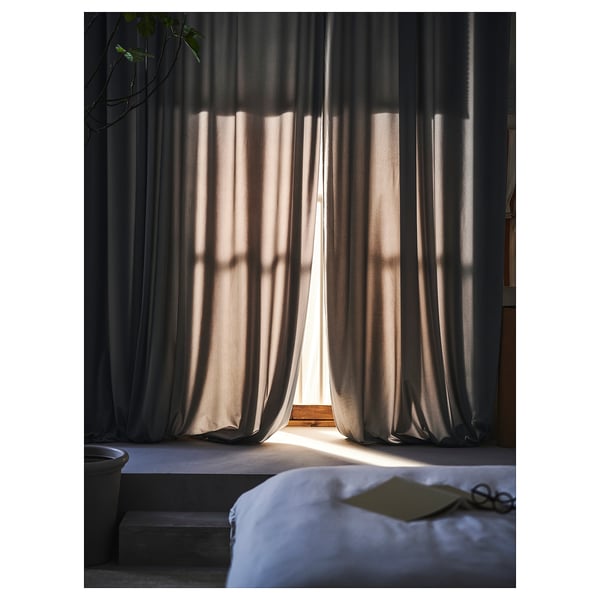 Gray curtains let sunlight into bedroom with bed, book, and plant.