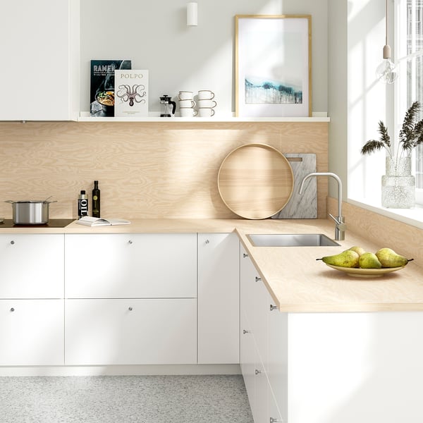 Modern kitchen with light wood counter, white cabinets, stainless sink. Green apples in bowl.