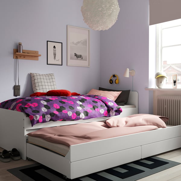 Modern bedroom with SLÄKT bed, colourful bedding, pull-out bed. Purple walls, art, rug, lamp, headphones.