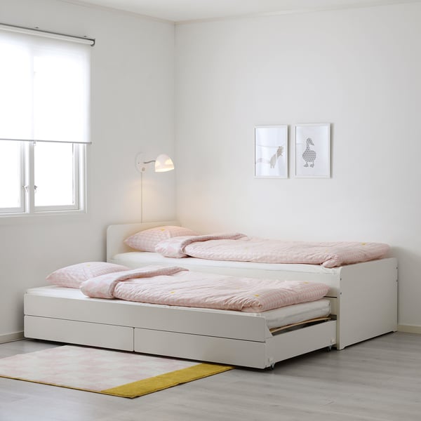 Bright white SLÄKT dual bed with pink linens, wall-mounted reading lamp, small frames, light rug, simple, minimalist design, fits well in small rooms.