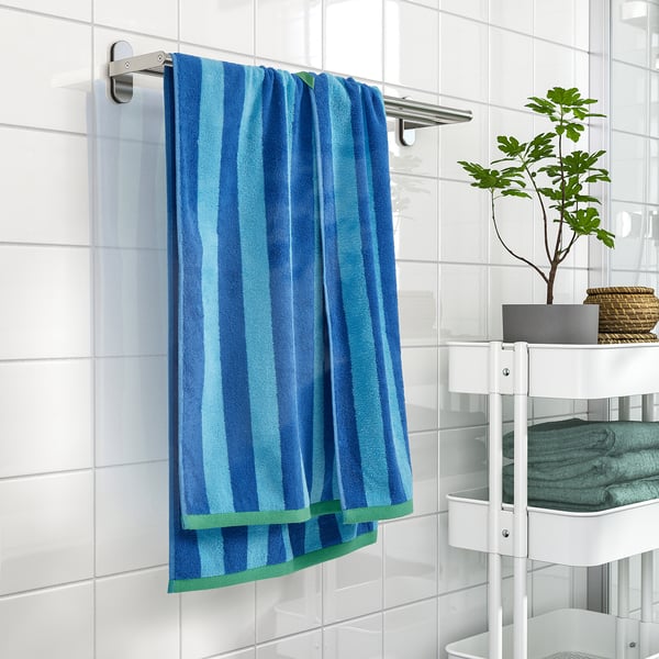 Blue & green striped towel hangs on rack, surrounded by white tiles and storage.