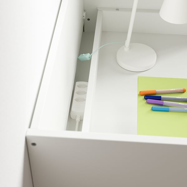 White desk with three open drawers, highlighting internal storage. Colourful pens on a green pad and a lamp on top, illustrating workspace use.