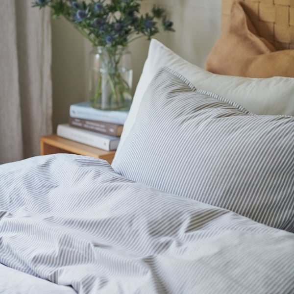 Striped duvet on bed with flowers and books.