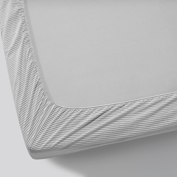 Corner of crisp, white fitted sheet on mattress, showcasing elastic edges for secure fit.