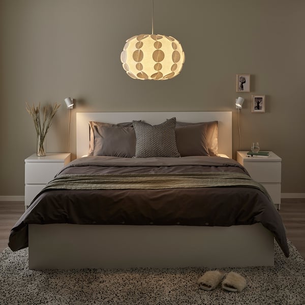 Modern cosy bedroom with grey bed, round light, & slippers.