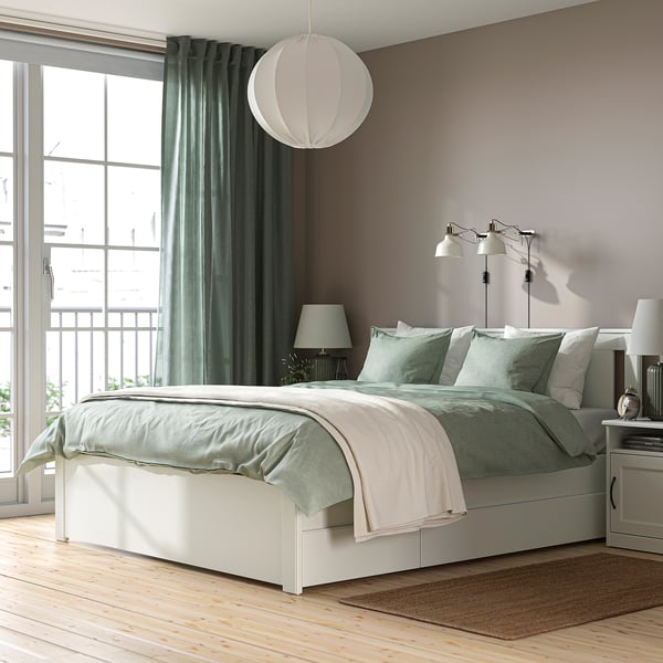A modern bedroom with grey SONGESAND bed, green curtains, under-bed storage, pendant light, nightstands, and a rug.